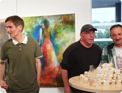 Photo prise pour la page galerie du plasticien Pierre Quentel lors du vernissage de l'expo au Roudour, on voit dans la photo Pierre avec Dominic Kerriou et Dominique Fouillard et devant eux une table pleine des petites boites ou se trouve la clé des chanson de l'artiste