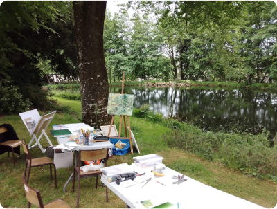 Photo prise lors d'un atelier animé par le plasticien Pierre Quentel, dans cette photo on voit un chevalet sur lequel on a posé une toile et des tables pleins d'outils de peinture comme les pinceaux, les tubes et des papiers posées sur des tables blanches