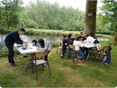 Photo prise lors d'un atelier animé par le plasticien Pierre Quentel, dans cette photo on voit des enfants autour de deux tables entrain de faire de la peinture et avec le peintre