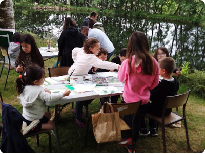 Photo prise lors d'un atelier animé par le plasticien Pierre Quentel, dans cette photo on voit des enfants autour d'une table entrain de faire de la peinture avec leurs parents