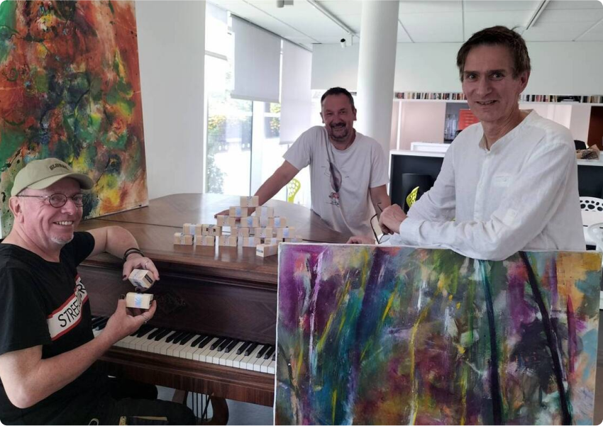 Phot prise pour la page galerie du plasticien Pierre Quentel lors de l'expo au Roudour avec l'artiste Dominic, on voit pierre derrière une de ses toiles, et les collaborateurs un derrière le piano et l'autre assis