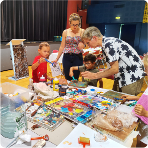 Phot pour la galerie du plasticien Pierre Quentel, dans cette photo on voit un groupe d'enfants qui entoure le peintre lors d'un atelier animé par lui, et on le voit entrain de montrer comment colorier à deux enfants ainsi que leur maman