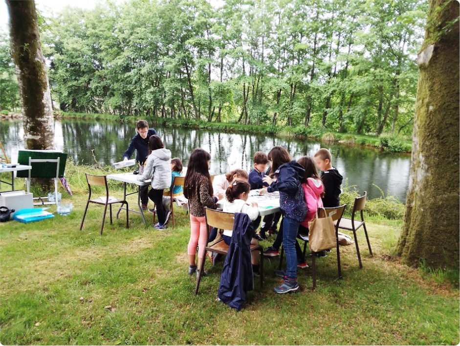 Photo prise pour la page cours de dessin morlaix , dans cette photo on voit un groupe d'enfants qui contourne une table en plein nature, entrain de faire un atelier de dessier et peinture animé par Pierre Quentel, et au fond, on voit le peintre entrain de préparer ces outils sur une autre table